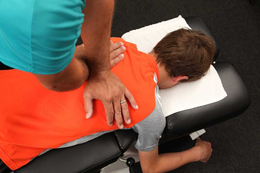 A person sitting on a couch with one hand supporting their lower back, wincing in discomfort.